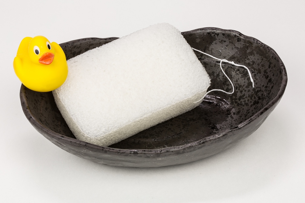 Gelbe Gummiente und weißer Badeschwamm in einer schwarzen Schale.