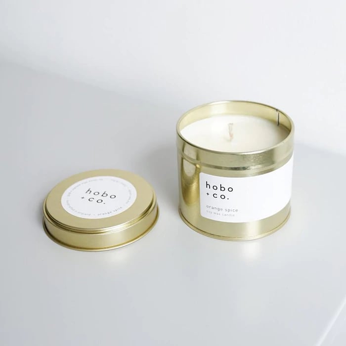 Goldene Duftkerze 'hobo + co.' mit abgenommenem Deckel auf weißem Hintergrund.