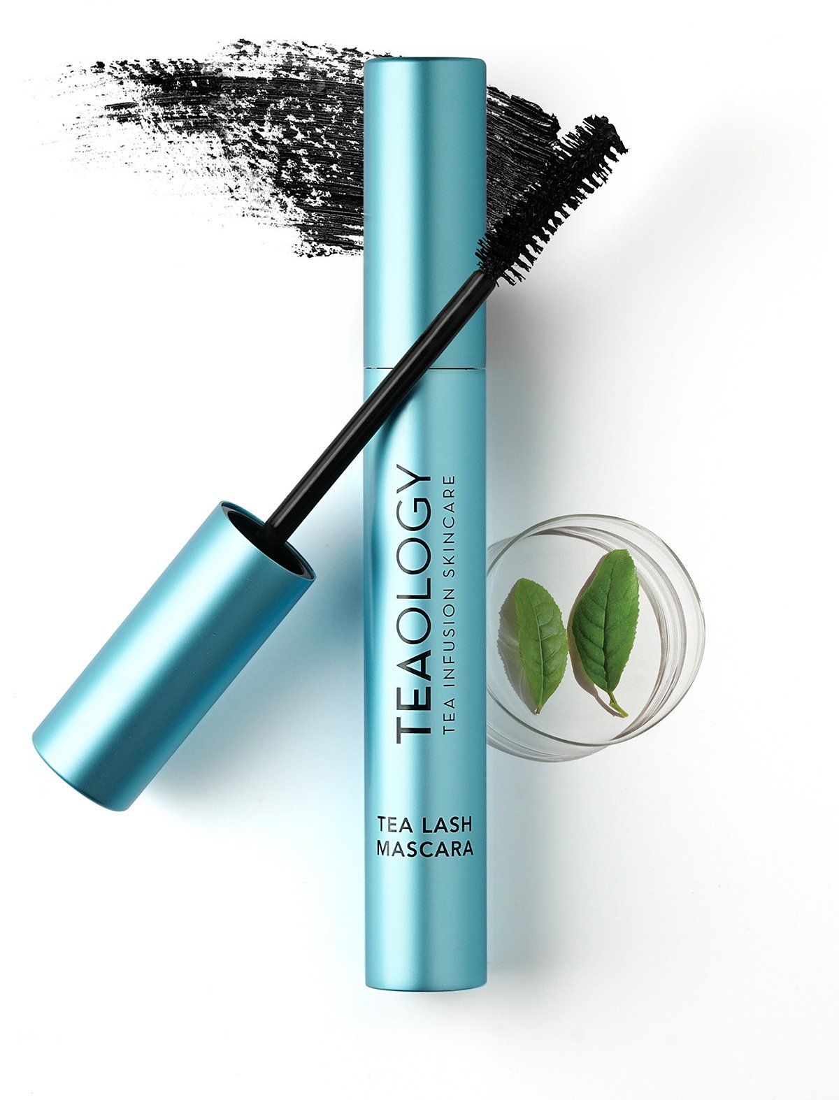 TEAOLOGY Tea Lash Mascara in türkisfarbener Tube, geöffnet, mit Pinsel und Teeblättern im Hintergrund.