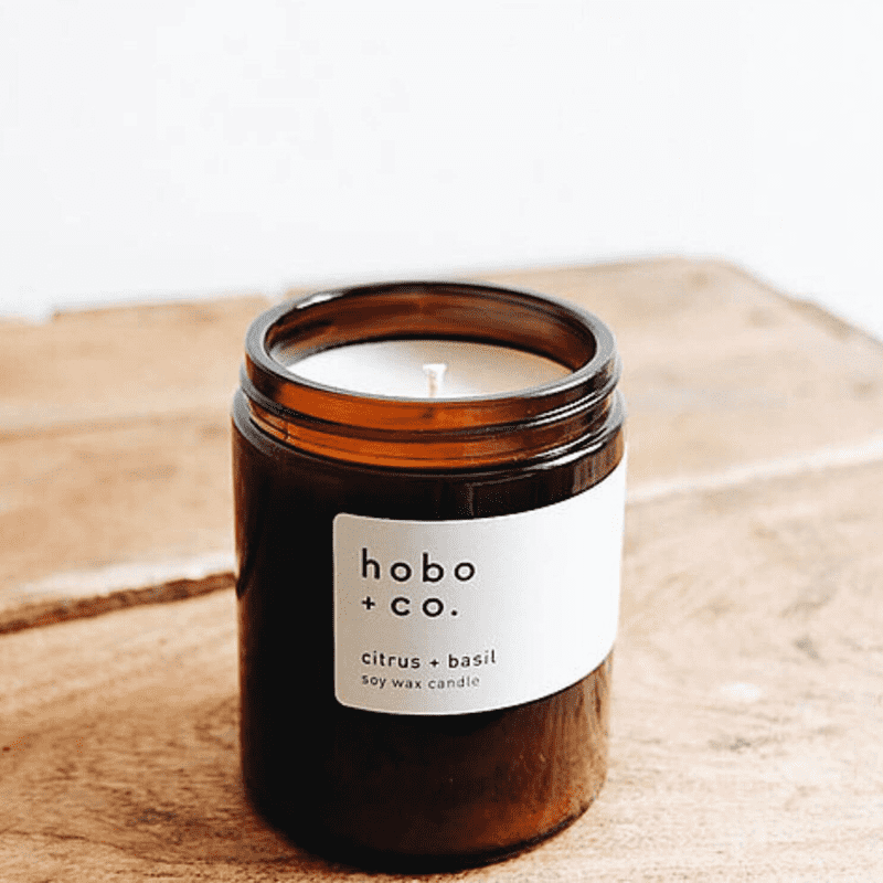 hobo-co-citrus-basil-essential-oil-candle-180ml_optimized Braunes Glas mit hobo + co. Zitrus-Basilikum Sojawachskerze auf einem Holztisch.