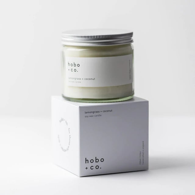 02766335-87A1-4277-8D6B-8E27B331EAF3 Kerze im Glas mit Zitronengras-Kokosduft von hobo + co. auf einer weißen Verpackung.